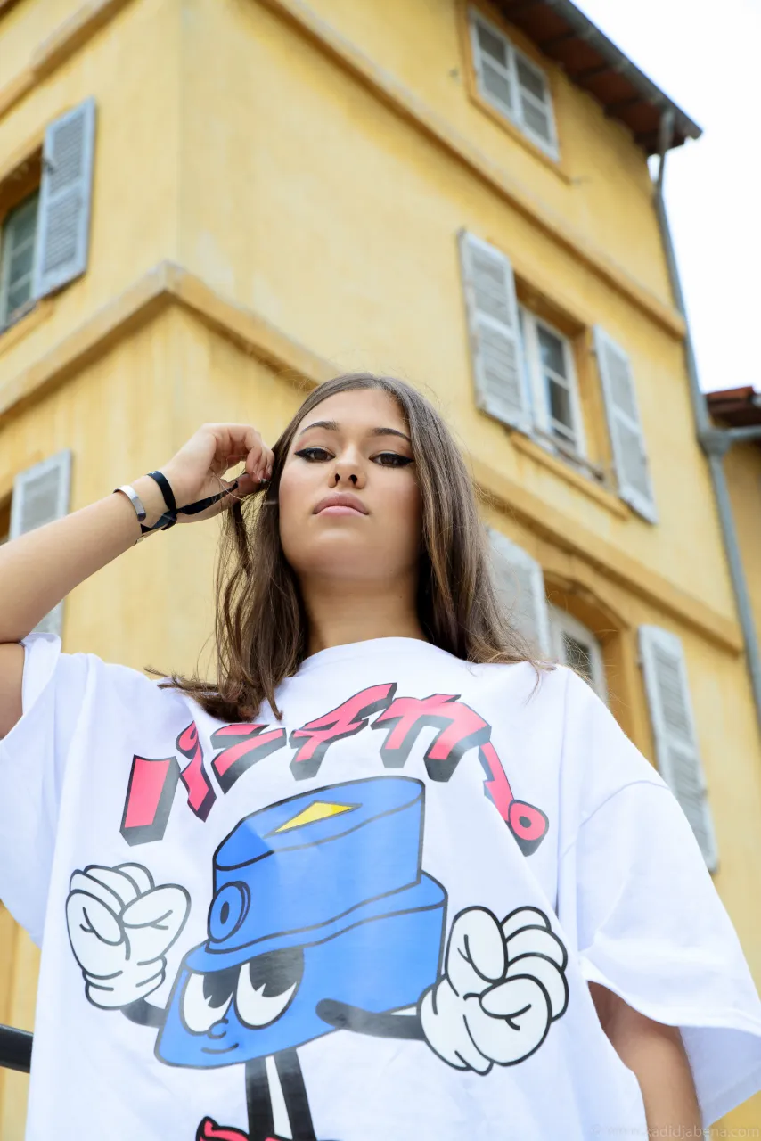 Jeune femme en t-shirt imprimé devant une façade jaune, Studio Bena